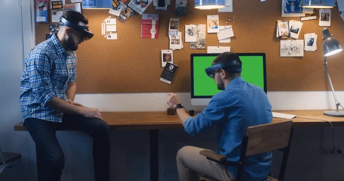 Young adult Caucasian colleagues using holographic augmented reality glasses together, creating a model on a computer screen. Green screen chroma key. 4K UHD RAW edited footage