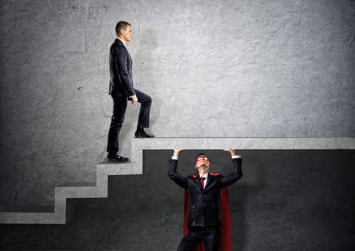 A businessman in a red cape holding a concrete floor and stairs for another businessman to step on.
