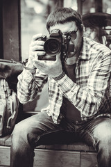 A man hipster style with a camera in center of Europe. Human have a hobby photography