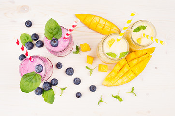 Freshly blended yellow and violet  fruit smoothie in glass jars with straw, mint leaves, mango...