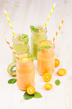 Freshly blended orange kumquat and green kiwi fruit smoothie in glass jars with straw, mint leaf, cut ripe berry, close up. White wooden board background, vertical.