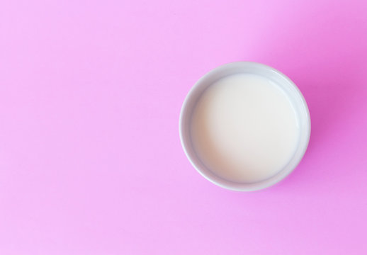 Closeup top view milk in white ceramic cup on pink background, selective focus