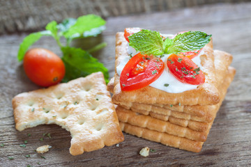 Cracker topped with cream cheese, tomato and mint on wooden background