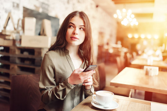 Pretty girl using cell phone smiles and looks over her shoulder out of frame.In caffe.With coffe.