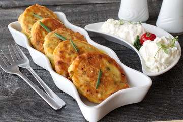 Fritters with fresh green onion and pieces of boiled egg on a white plate with fresh greek yoghurt on a dark wooden background. Healthy breakfast. Healthy eating concept © Olena