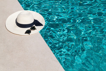 Fototapeta na wymiar Hat and sunglasses at the side of swimming pool, summer travel concept the side of swimming pool, summer travel concept