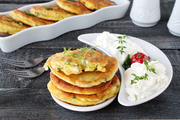 Fritters with fresh green onion and pieces of boiled egg on a white plate with fresh greek yoghurt on a dark wooden background. Healthy breakfast. Healthy eating concept