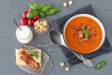 Thick tomato soup with basil and fried bacon in a black ceramic bowl on a grey abstract background. Healthy eating concept Fresh tomato soup with creme fraiche
