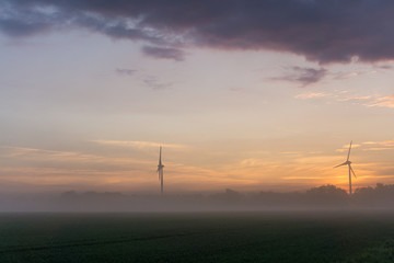 Fototapeta premium wind wheels at sunrise and fog with dark clouds