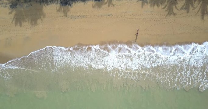 Aerial footage of a tropical beach with waves and a couple walking on the beach, panning out above view. Summer vacation holiday.
