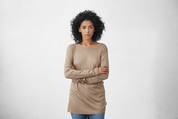 Indoor studio shot of angry young dark-skinned housewife in casual clothes standing in closed...