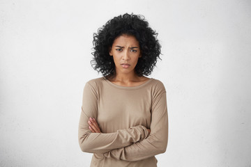 Angry annoyed young housewife keeping arms crossed and staring at camera with sceptical and...