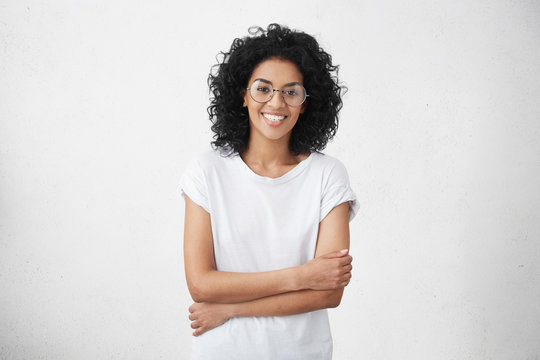 Human facial expressions, emotions, feelings, reaction and attitude. Attractive happy mixed race girl wearing her shaggy hair loose, holding arms folded in front of her, rejoicing at good news