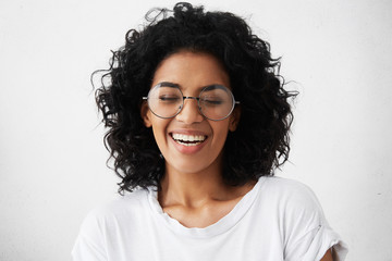 Pretty girl with dark clean skin and beautiful toothy smile laughing out loud at funny joke while...