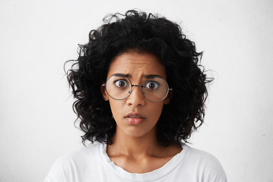 Human emotions, feelings, reaction and attitude. Startled mixed race girl wearing big round glasses looking at camera with shocked expression, afraid of sudden noise while staying home alone