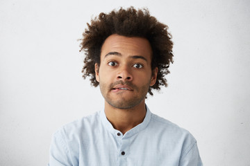 Headshot of attractive mixed race male student with stubble and tousled hair biting his lower lip...
