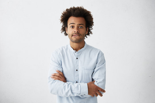 Scared young Afro American man in casual shirt keeping arms folded, biting lips, feeling nervous and impatient while waiting for his wife giving life for their first child. Human emotions and feelings