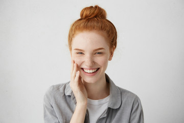 Youth and happiness. Close up view of beautiful Caucasian teenage woman with long ginger hair and freckles, dressed casually, standing against blank gray wall. Horizontal, isolated, studio shot, model