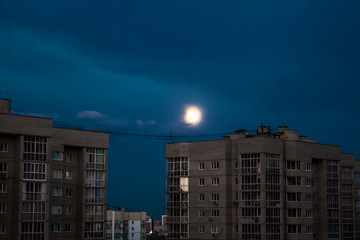 Gloomy sky with buildings and with the moon in the evening, over the city