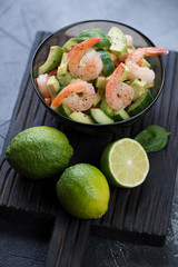 Bowl of avocado salad with shrimps and cucumber on a black wooden serving board, vertical shot