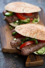 Close-up of pitas with bbq cevapi or cevapcici sausages and vegetables, vertical shot