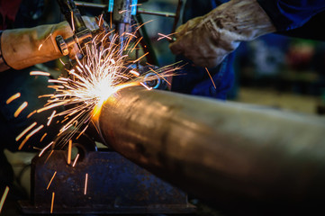 Worker cutting steel pipe with acetylene welding cutting torch and bright sparks in steel...