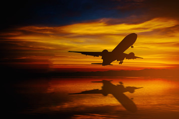 Silhouette of plane fly over sea on dramatic sky during sunset.