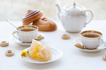 Cups of tea with honey on a plate and teapot, white baackground