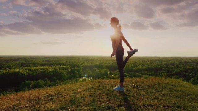 Young woman doing stretching exercise in an epic beautiful place at sunset. Beautiful glare from the sun, the top of a green hill. Health and a healthy lifestyle