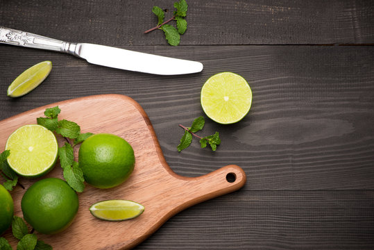Fresh limes on cutting board on wooden table. Top view, background.