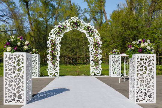 White lace wedding arch and chairs for guests. Vases with purple flowers. The wedding ceremony area at the wedding