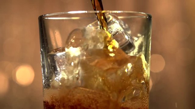 Cola poured into glass with ice on a flickering background.. Cola and ice in glass. Bubble float. Slow motion 240 fps. Slowmo. Full HD 1080p.