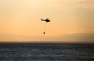 The helicopter collects water from the sea to extinguish a fire