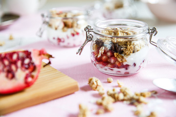 Diet dessert with yogurt, granola and pomegranates in a glassware. Horizontal. Rose tablecloth, silver spoon, wooden board.