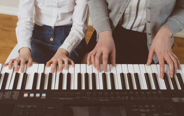 Woman teaching little girl to play the piano.