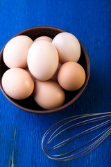 Fresh eggs in a brown bowl on  blue background. Top view