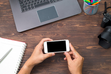 Vintage hipster wooden desktop top view with laptop, vintage camera, plant and touch screen tablet, male hands using a mobile phone