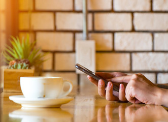 Close-up man sitting in cozy cafe and drinking coffee, of male hand using modern smart phone in cafe shop, blurred background, shallow DOF