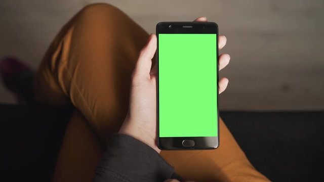 Handheld shot of female teen hands using smartphone with green screen sitting near window, uhd prores footage