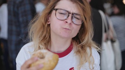 Cute millenial teenager in a trendy hipster outfit enjoys a huge donut on a food festival from artisan foodtruck, she makes a big bite and dances in satisfaction