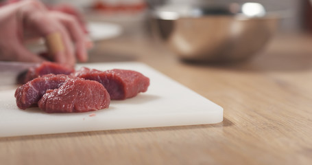 young female hand cutting raw beef with a knife on plastic board, 4k photo