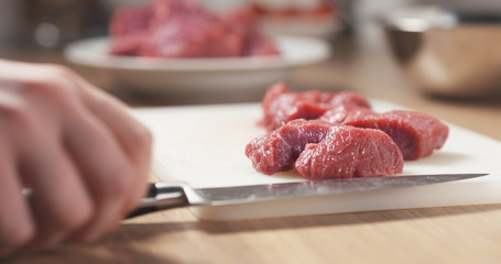 young female hand cutting raw beef with a knife on plastic board, 4k photo
