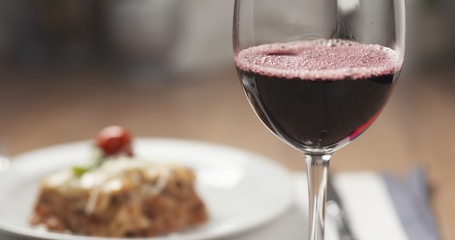 pouring red wine in glass with lasagna at background, 4k photo