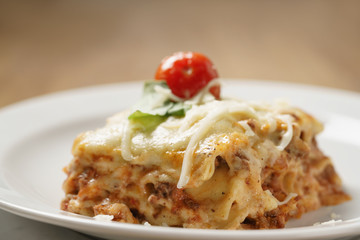 homemade lasagna portion on white plate on wood table, shallow focus