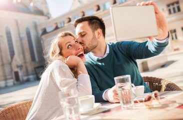 Dating. Young couple drinking coffee and having fun with tablet in the cafe. Love, dating, technology, lifestyle