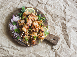 Grilled pork skewers with pickled red onion and mint on a rustic cutting board on a paper...