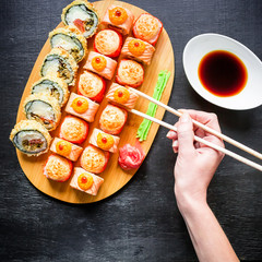 Fototapeta na wymiar Sushi rolls, sauce, ginger, wasabi and woman hand holding chopsticks on dark background. Top view. Flat lay.