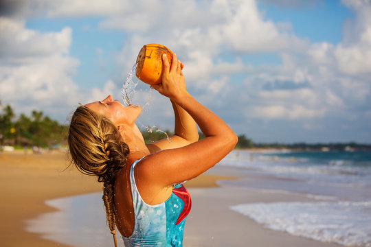 A Woman Drinks Coconut At The Seashore At Sunset