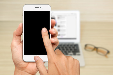 Hand Hold and touch on white Smartphone with laptop background