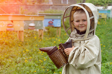 The boy in protective clothing beekeeper works on an apiary. Apiculture.